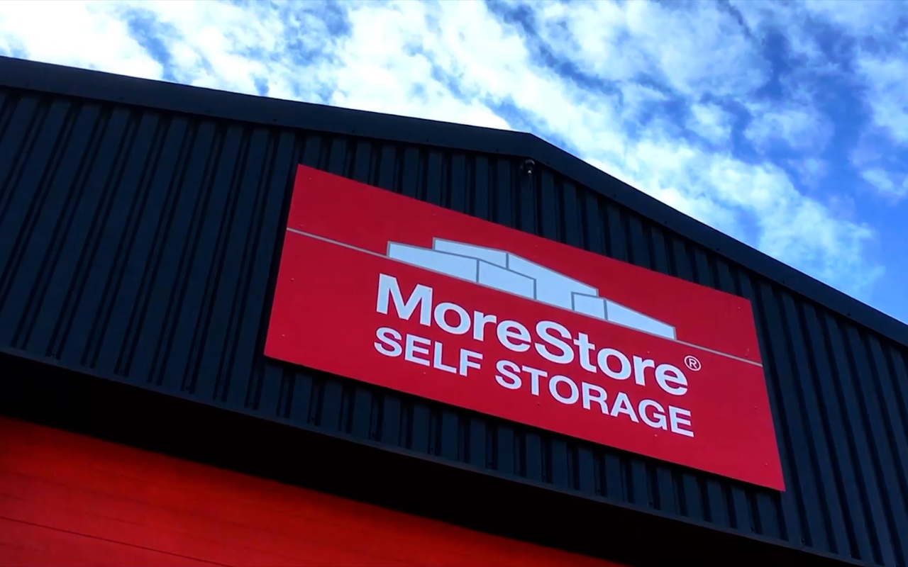 MoreStore Self Storage exterior sign on a building under a blue sky.
