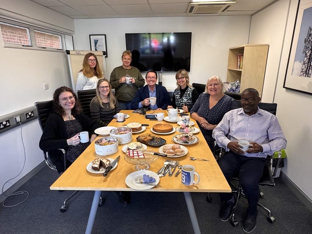 Staff in a meeting room eating cake and drinking tea to raise money for World Mental Health Day